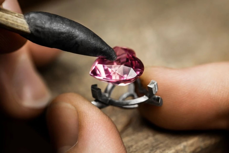 Close-up of a pink gemstone being held by fingers with a specialized tool, showcasing jewelry making and precious stone work.
