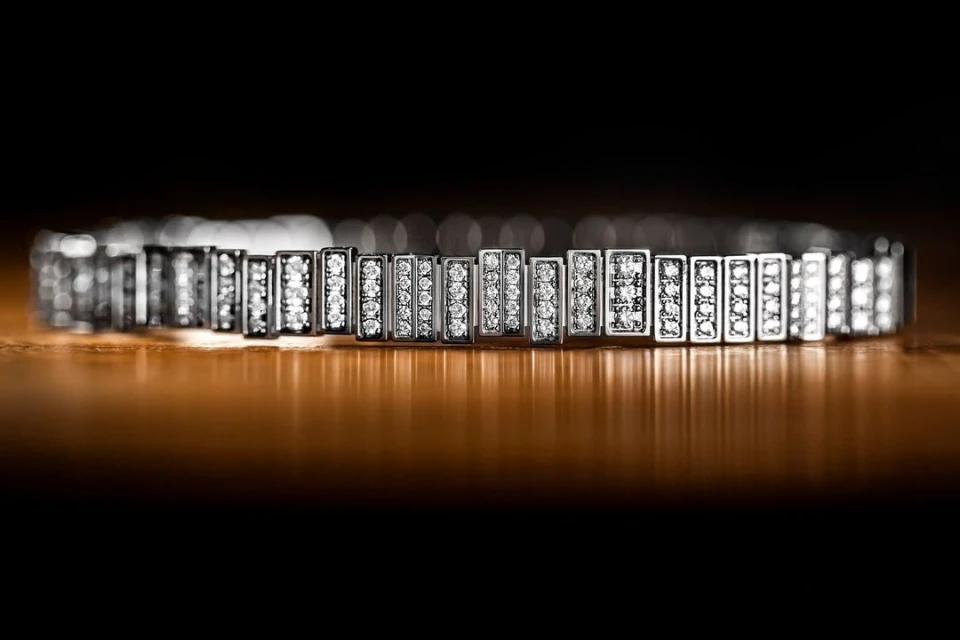 Close-up of a sparkly, platinum, diamond bracelet featuring a geometric design, reflecting light on a brown surface against a dark backdrop.
