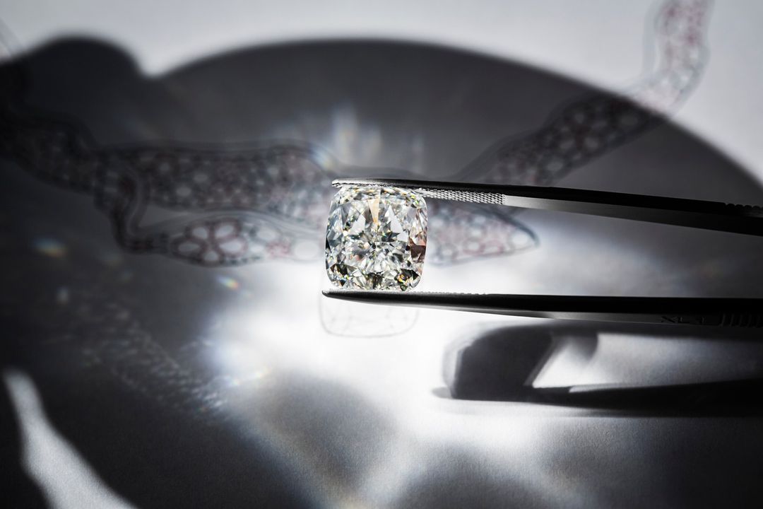 Close-up shot of a radiant cushion-cut diamond held by tweezers, set against a backdrop of abstract shadow patterns and lens flares.