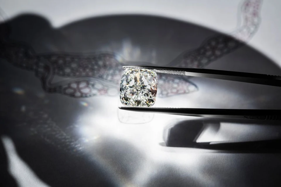 Close-up shot of a radiant cushion-cut diamond held by tweezers, set against a backdrop of abstract shadow patterns and lens flares.