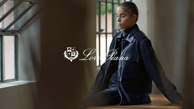 Woman with braided hair wearing a dark denim jacket seated indoors near gridded windows, photographed by Pol Baril.