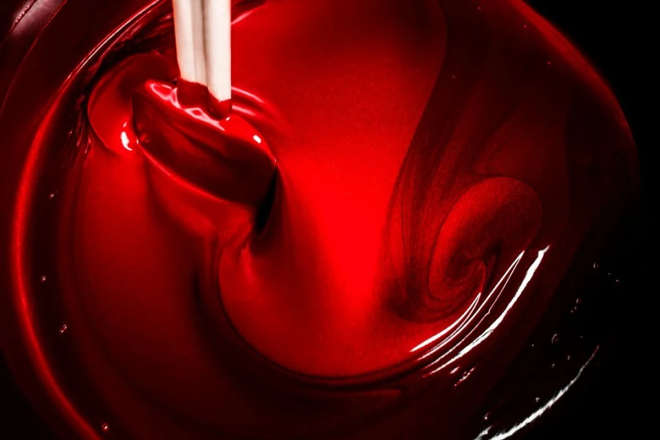 Close-up of vibrant red liquid being stirred with a white stick, creating dynamic swirls and textures against a dark background.