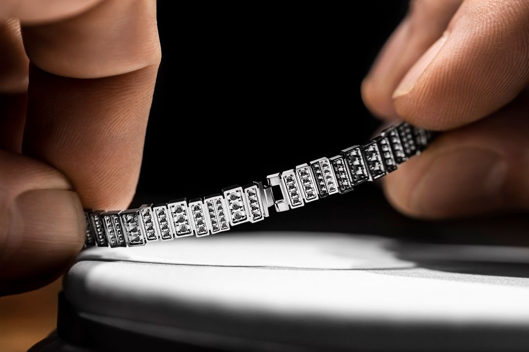 Close-up of a silver bracelet with black stones being held by two hands against a black background, showcasing jewelry fashion.