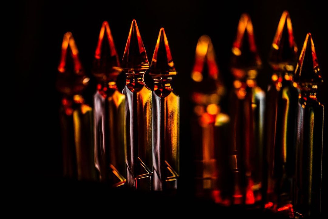 Close-up shot of many glass ampoules lined up in rows against a black background, highlighted by warm-toned, dramatic lighting.