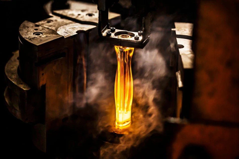 Close-up shot of an industrial machine processing hot molten glass, with a dark background and selective focus, creating an intense and fiery atmosphere.