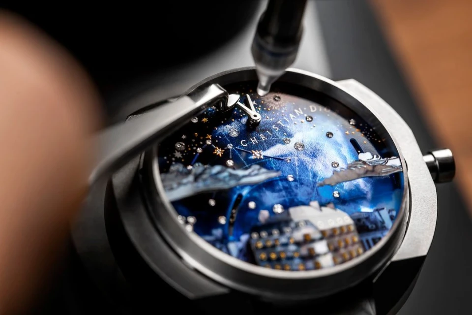 Close-up of watch assembly: a jeweler uses tools to set gems on a Dior timepiece showcasing an elaborate city and constellation dial.