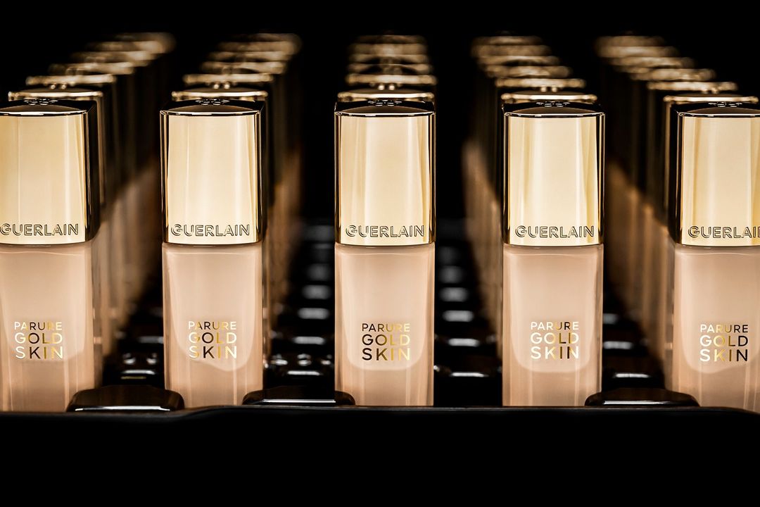 Several bottles of Guerlain Parure Gold Skin foundation are neatly arranged in rows, featuring gold lids and beige-tinted containers.