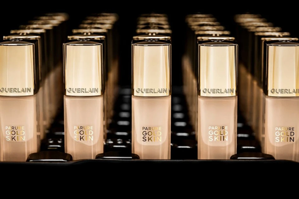 Several bottles of Guerlain Parure Gold Skin foundation are neatly arranged in rows, featuring gold lids and beige-tinted containers.