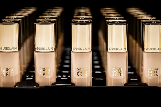 Several bottles of Guerlain Parure Gold Skin foundation are neatly arranged in rows, featuring gold lids and beige-tinted containers.