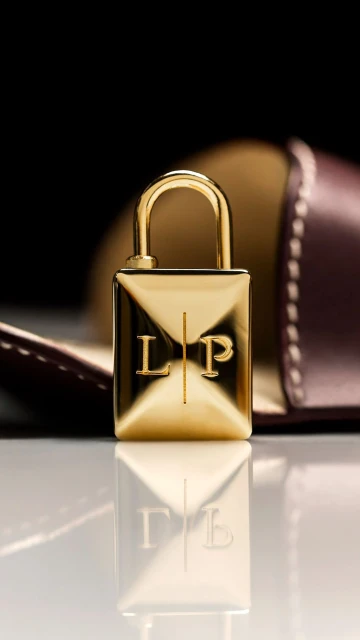 Close-up studio shot of a gold-colored padlock with the letters 'LP' on its face, displayed on a glossy surface with a blurred background.