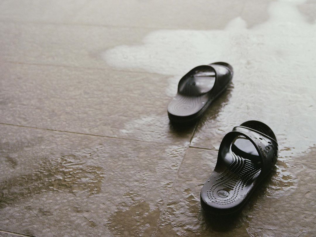 Two black rubber slides sit on a light grey tiled floor with a shiny wet surface, positioned in the lower right and upper left of the frame.