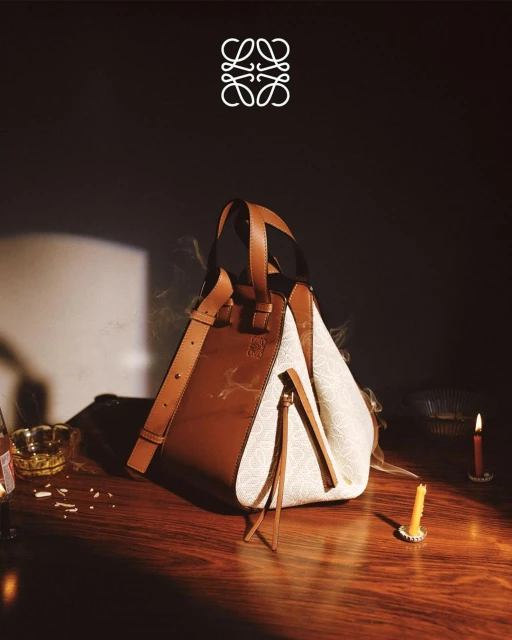 Loewe handbag in brown leather and patterned fabric, presented with vintage style on a wooden table with lit candles.