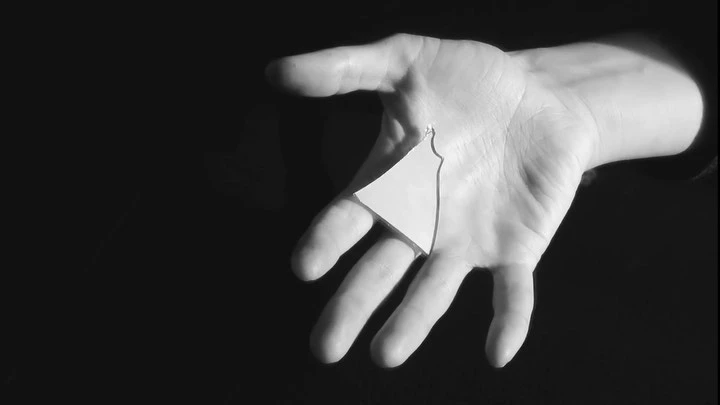 Hand holding a geometric paper shape in black and white against a stark black background, creating a high-contrast composition.