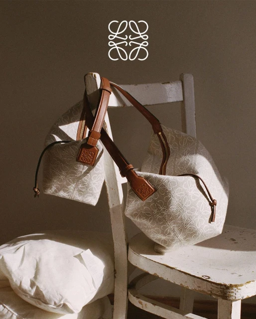 Still life shot of two LOEWE patterned bucket bags, one on a vintage white wooden chair with a white pillow on the seat.