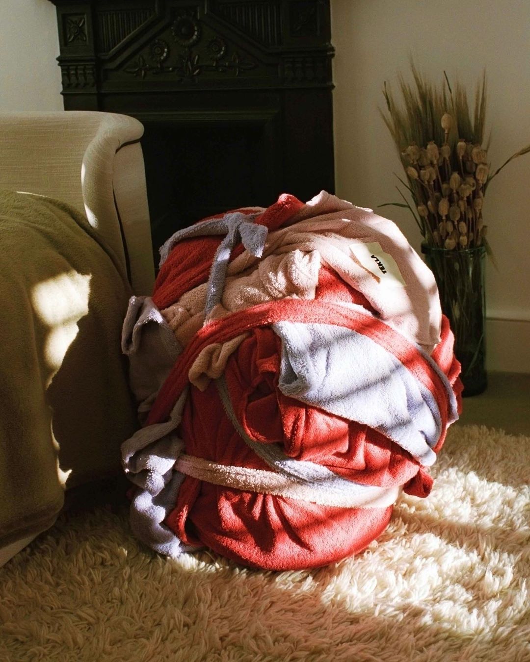 Pile of towels on a cream colored shaggy rug in a sunny interior, near a fireplace, with indirect natural light.