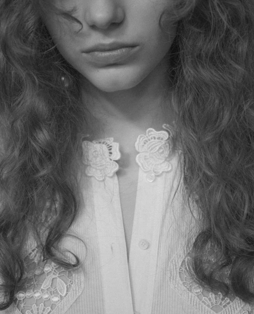 Close-up black and white shot of a young woman with wavy hair wearing a white shirt with lace detailing and decorative collar clasps.
