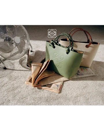 Loewe Puzzle Fold tote bags in green and beige displayed on a carpet with a floor fan and newspapers in the background.