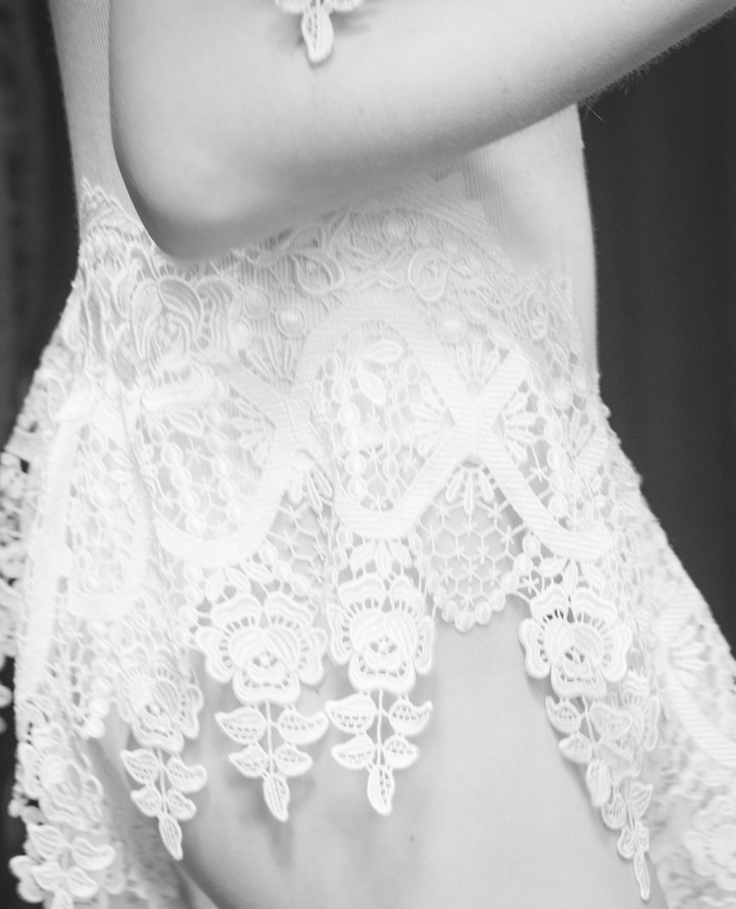 Close up of white lace trim on a garment worn by a person, captured in a monochrome photographic style.