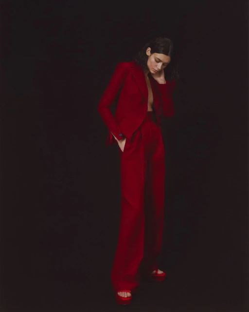 Elegant adult woman in a red suit posing against a black backdrop, showcasing fashion and style with a confident stance and modern attire.