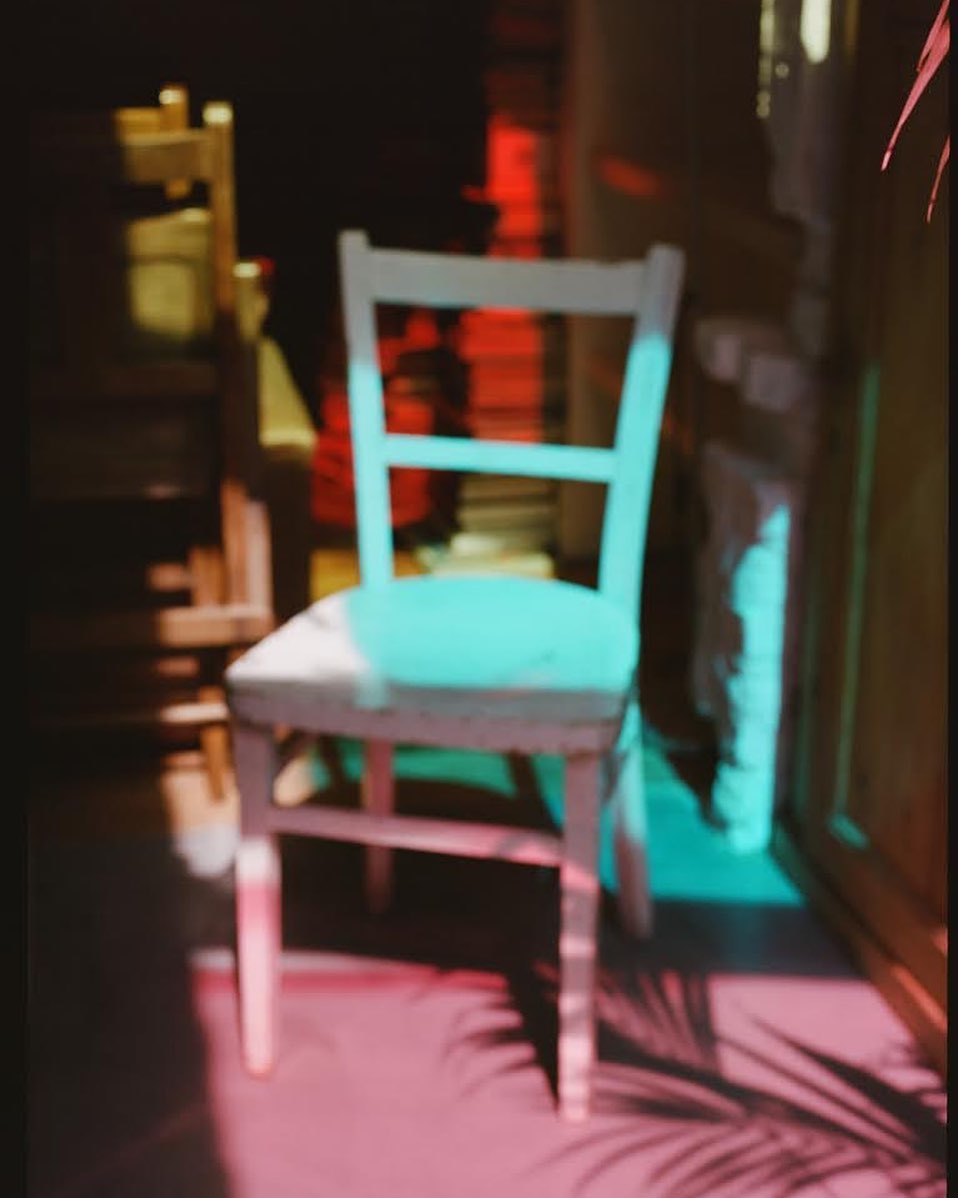 Wooden chair in room interior with pink and blue light creating shadows and highlights on chair and floor.