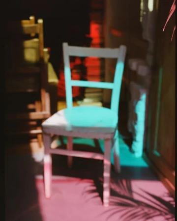 Wooden chair in room interior with pink and blue light creating shadows and highlights on chair and floor.