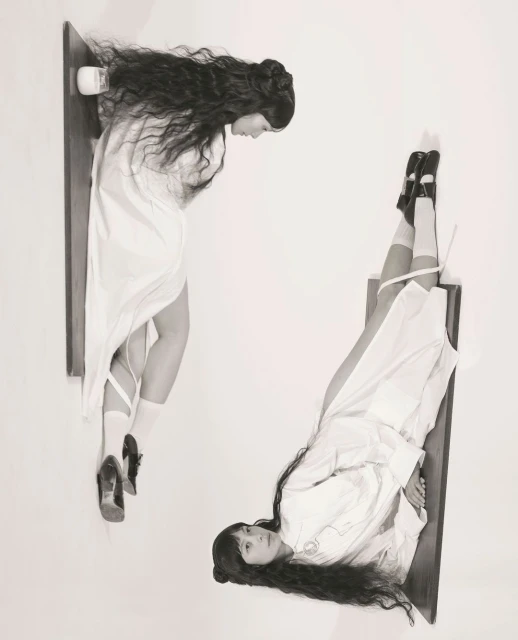 Black and white portrait features two women in white dresses, one looking down and the other looking up, floating on wooden shelves.