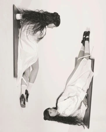 Black and white portrait features two women in white dresses, one looking down and the other looking up, floating on wooden shelves.
