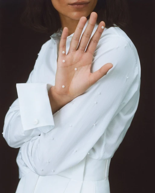 Woman in a white outfit with tiny pearls on her hand, posing against a dark backdrop, in a beauty and fashion-focused composition.