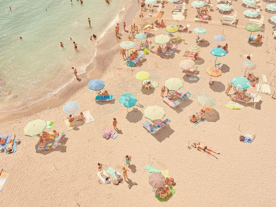 Aerial view of crowded sandy beach with colorful umbrellas, people sunbathing and swimming in the turquoise sea on a sunny day.