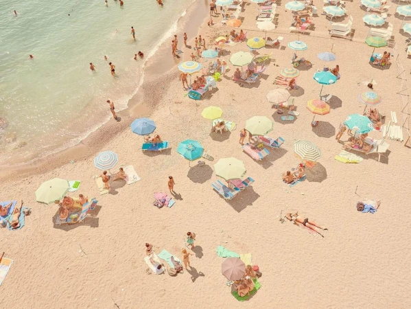 Aerial view of crowded sandy beach with colorful umbrellas, people sunbathing and swimming in the turquoise sea on a sunny day.
