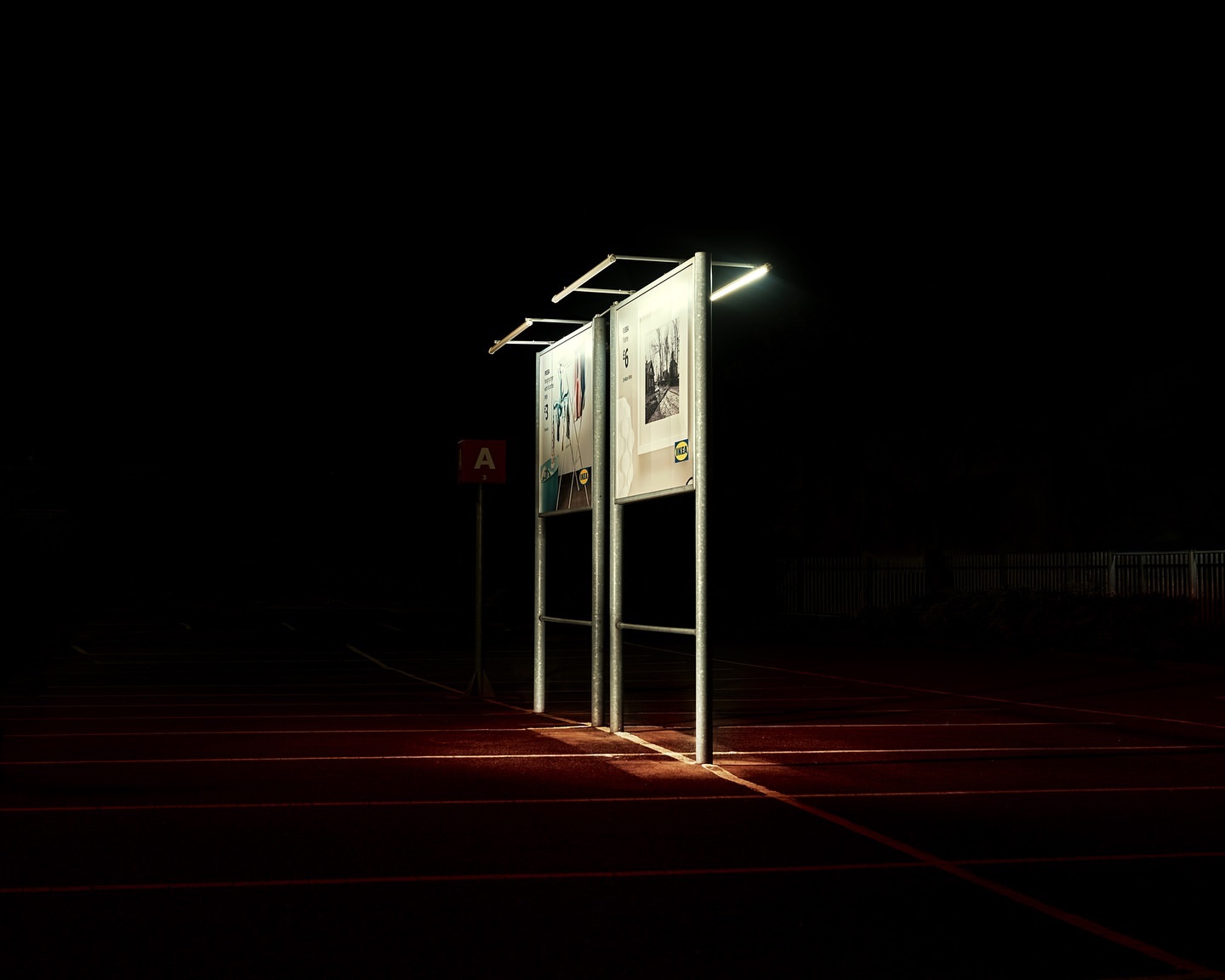 Illuminated bulletin boards stand on a track in the dark, creating a contrast of light and shadow with a sign in the background.