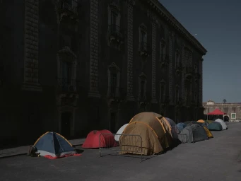 Multiple camping tents pitched in a paved plaza against the dark exterior facade of a large classic building in London