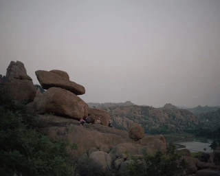 Distant figures resting among large weathered boulder formations under a hazy, pale sky photographed by Polly Tootal.