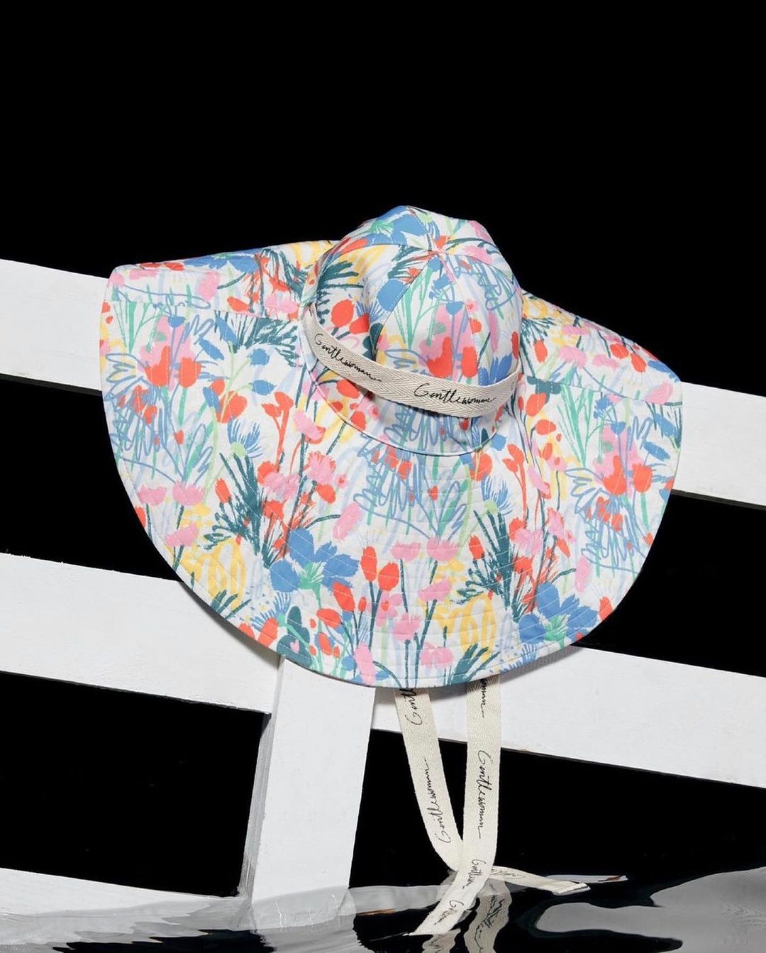 Floral sunhat with chin straps on a white railing, set against a black background. Fashionable sun protection for warm weather.