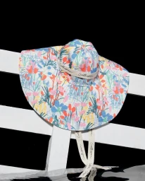 Colorful floral print sun hat with dangling ribbons resting on white wooden slats against black background