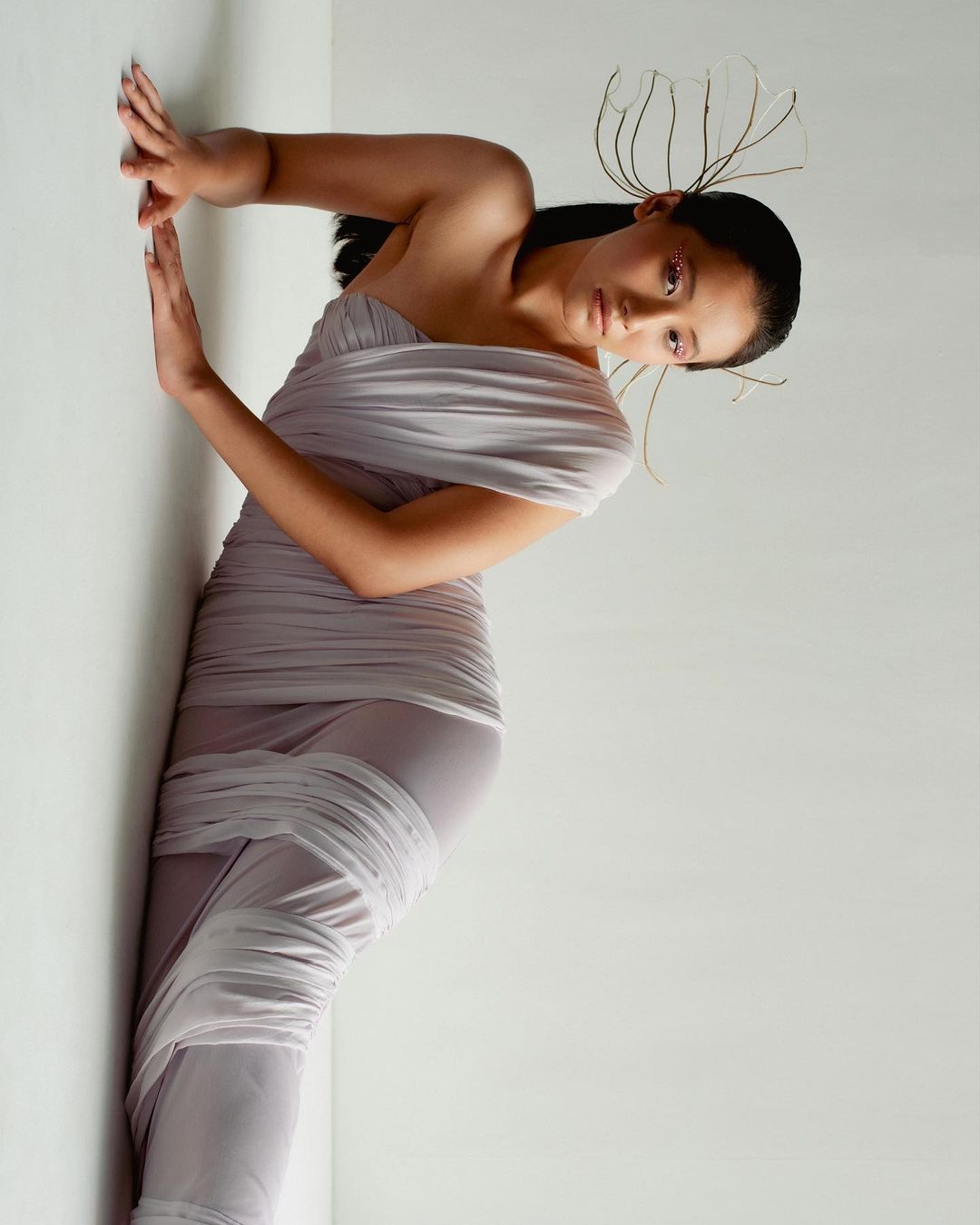 Elegant woman in lilac dress poses in a bright studio. Shoulder-up view shows hair accessories, stylish clothing, and neutral color palette.