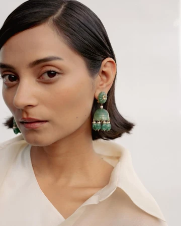 Close-up portrait of a woman wearing ornate green drop earrings and a white shirt against a plain light background