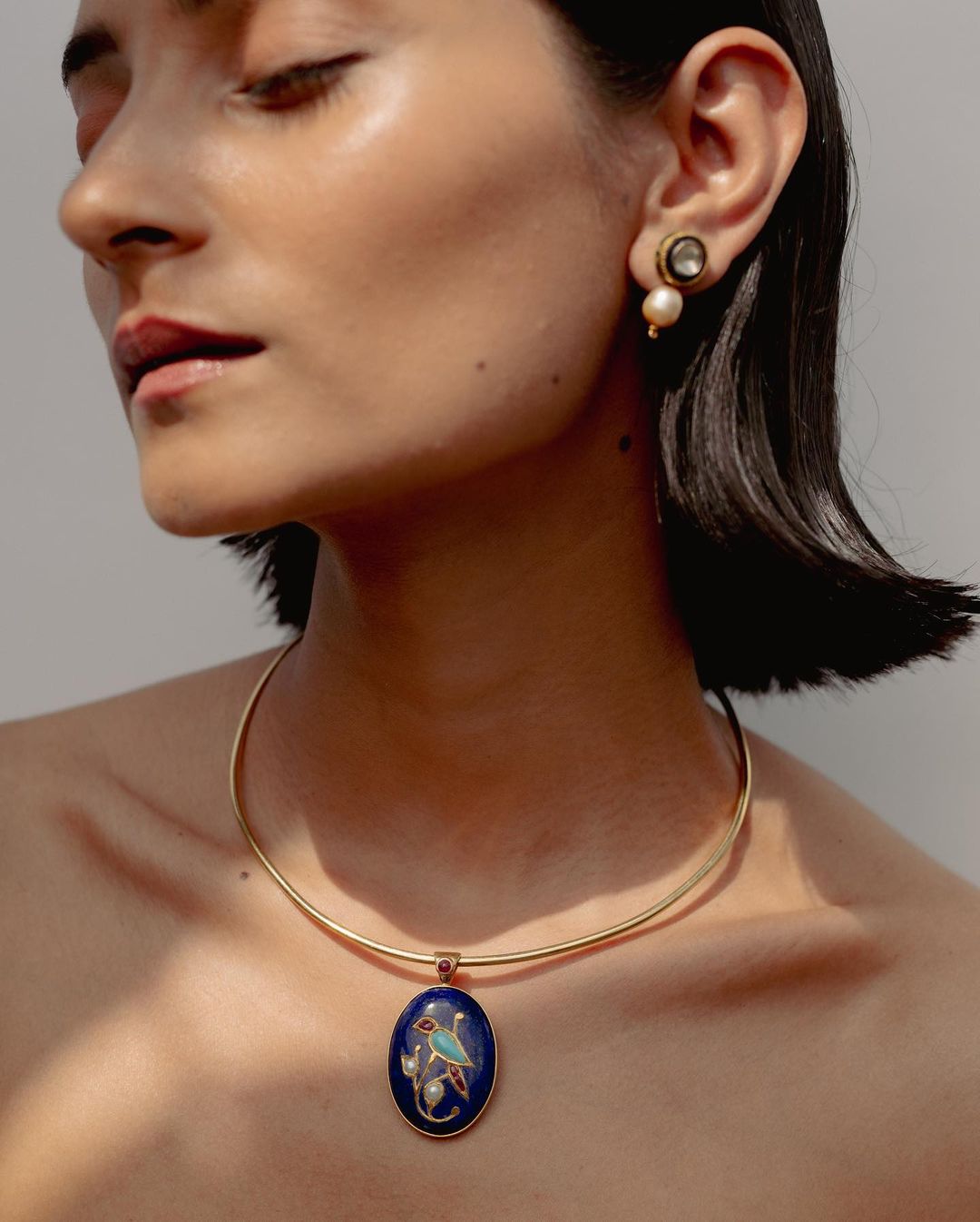 Close-up of a woman wearing gold necklace with blue stone pendant and pearl earrings, showcasing fashion jewelry and accessorizing.