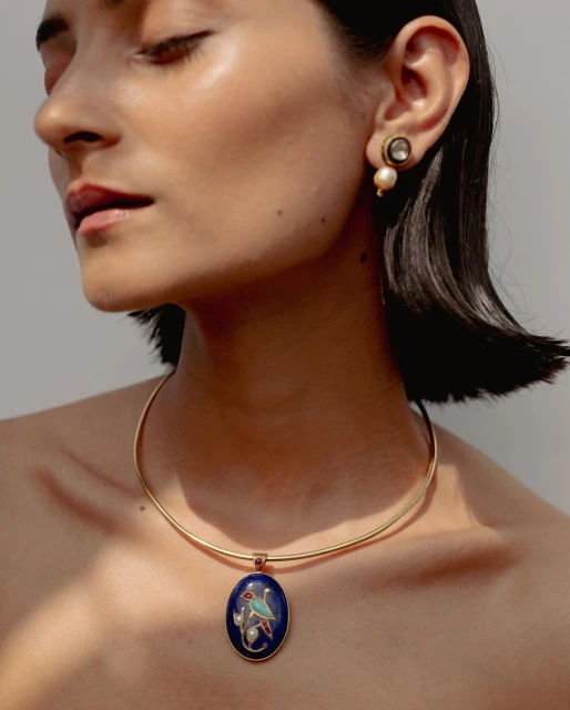 Close-up of a woman wearing gold necklace with blue stone pendant and pearl earrings, showcasing fashion jewelry and accessorizing.