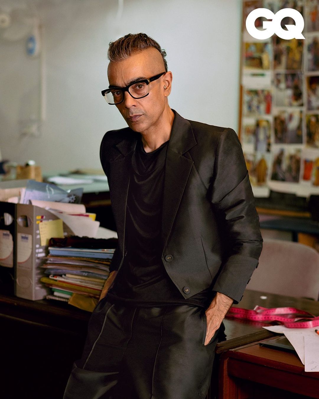 Middle-aged man in a dark suit and glasses poses indoors, looking seriously at the camera. Editorial fashion portrait for GQ.