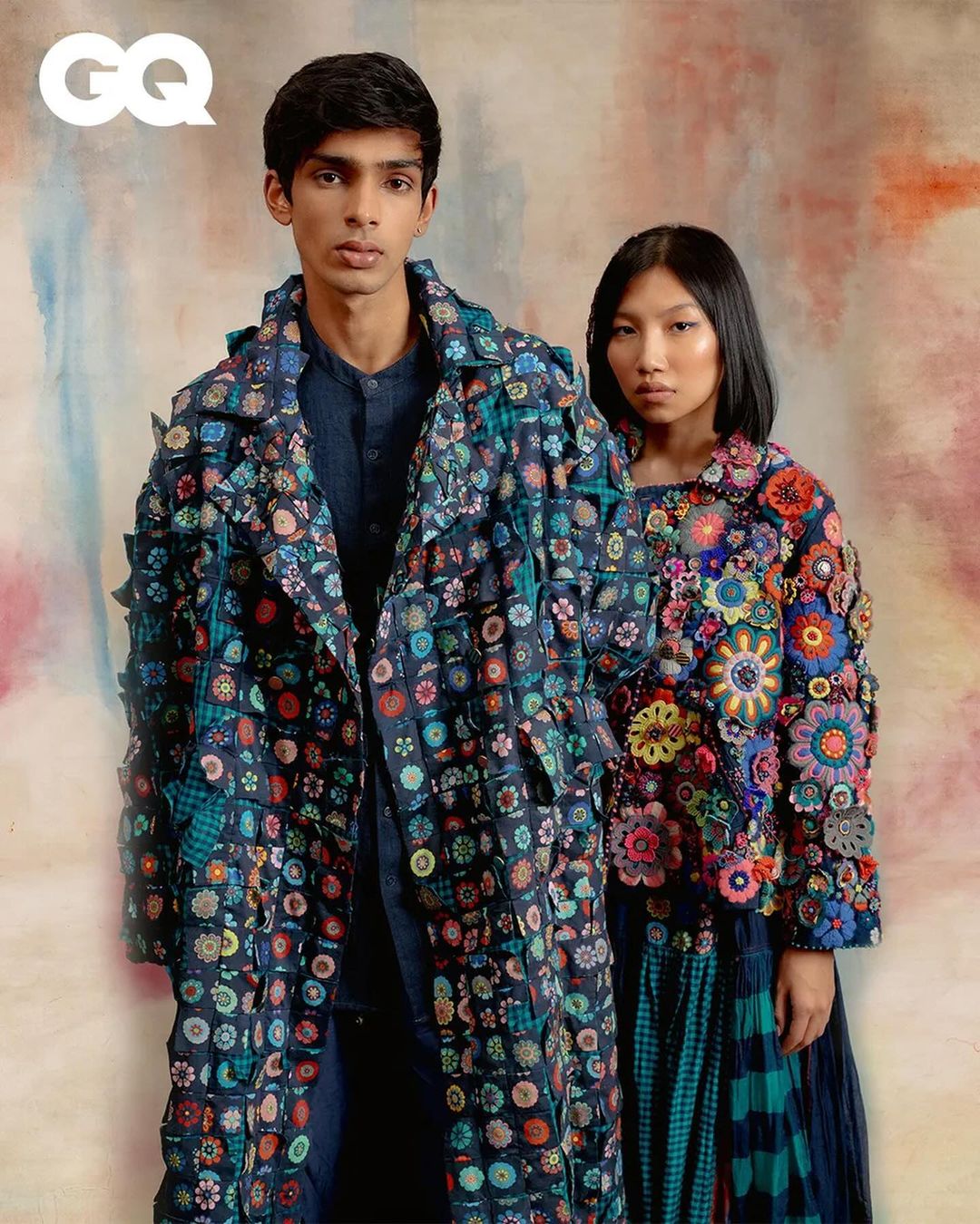 Editorial shot of two fashion models in a photo studio, wearing colorful floral-patterned outerwear, standing in front of a neutral backdrop.