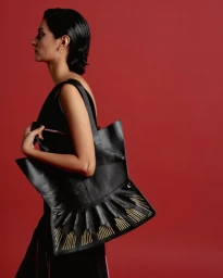 Profile view of a South Asian woman holding a black leather tote bag against a solid red background