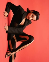 Woman in a black blazer and patterned leggings posing against a solid red studio background in Mumbai