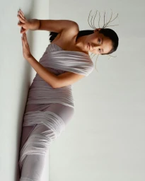 Woman in a draped lilac dress wearing a delicate wire headpiece against a white background, photographed by Prakrit Rai.