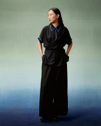 Model in black blouse with blue piping and black wide-leg trousers posing against gradient backdrop by Prakrit Rai