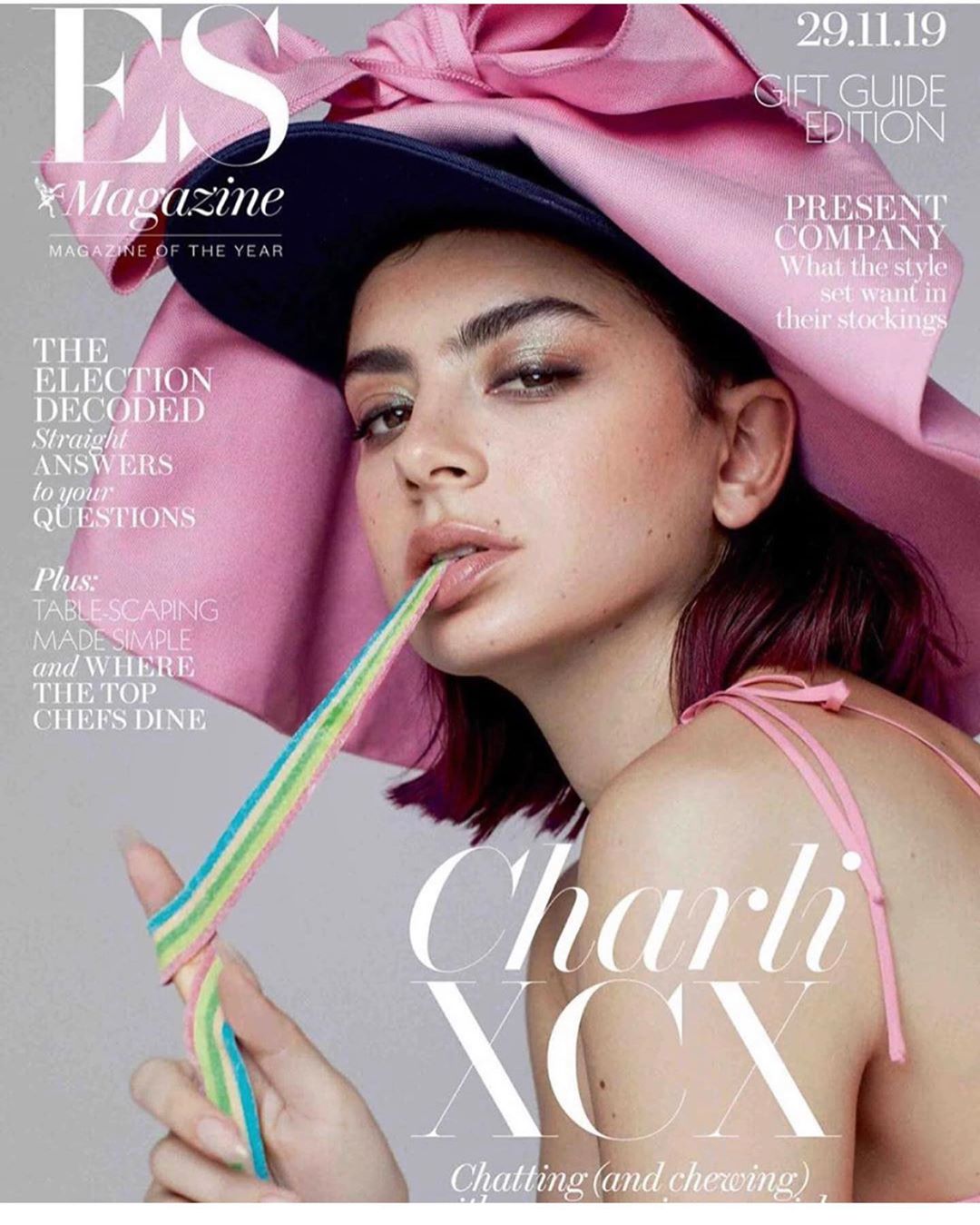 Magazine cover featuring Charli XCX in a pink hat, holding a rainbow candy strip, on a light background with magazine text overlays.