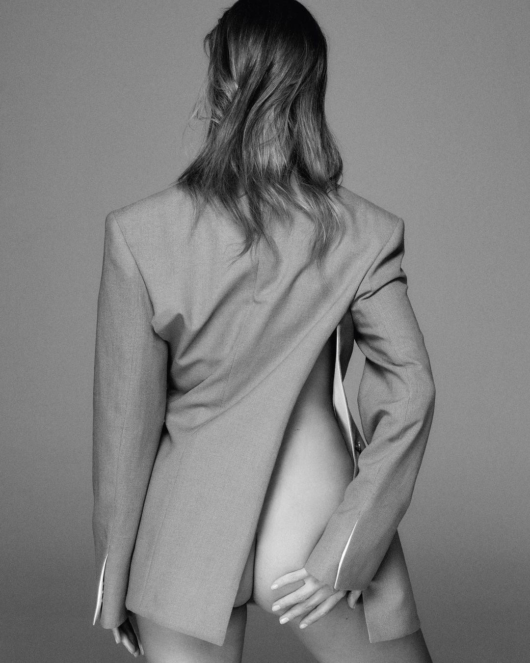 Monochrome portrait of a woman viewed from behind, wearing a tailored blazer backwards with bare back.