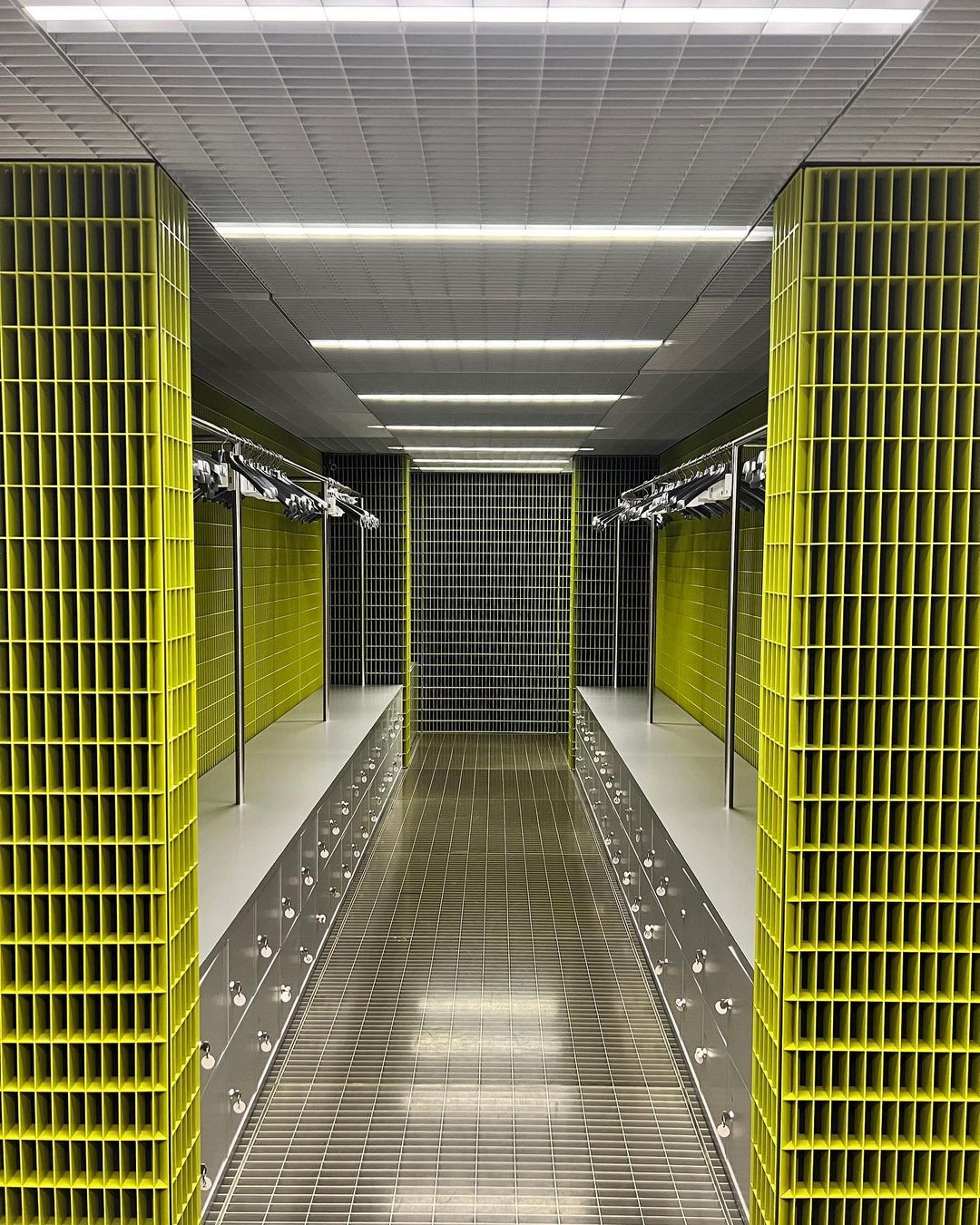 Architectural perspective of a changing room with yellow and gray lattice-like walls and a metal grate floor leading to a checkered wall.