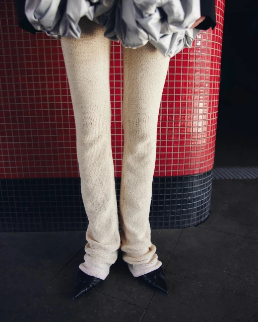 Fashionable leg warmers and pointed-toe heels worn indoors, standing against a red-tiled background for a chic, contemporary aesthetic.