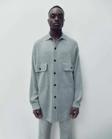 Fashion shot of a Black male model in a gray button-down shirt and matching pants against a neutral backdrop, showcasing minimalist style.